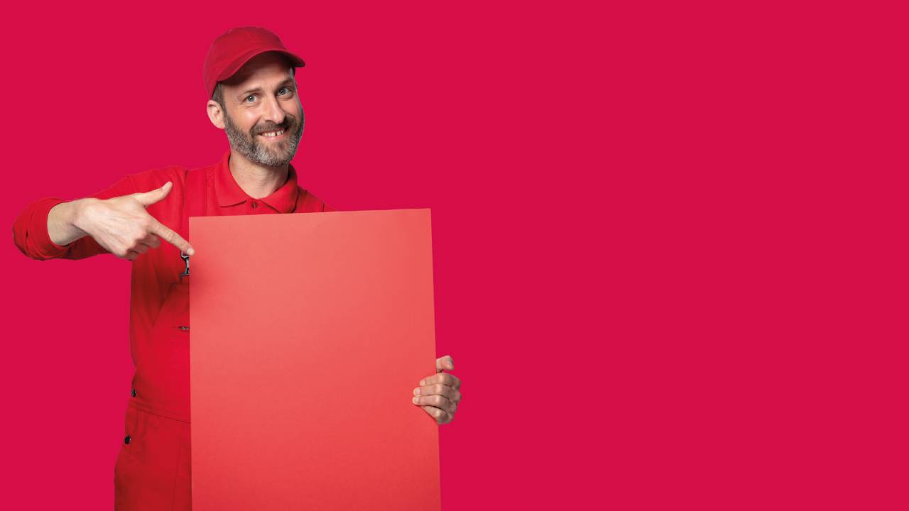 Bärtiger Mann in roter Arbeitskleidung präsentiert rotes Schild vor neutralem Hintergrund in magenta